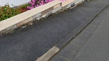 Ein weißes Gebäude mit einer blauen Tür, Hausnummer 24, und eine Steinmauer mit rosa Blüten.