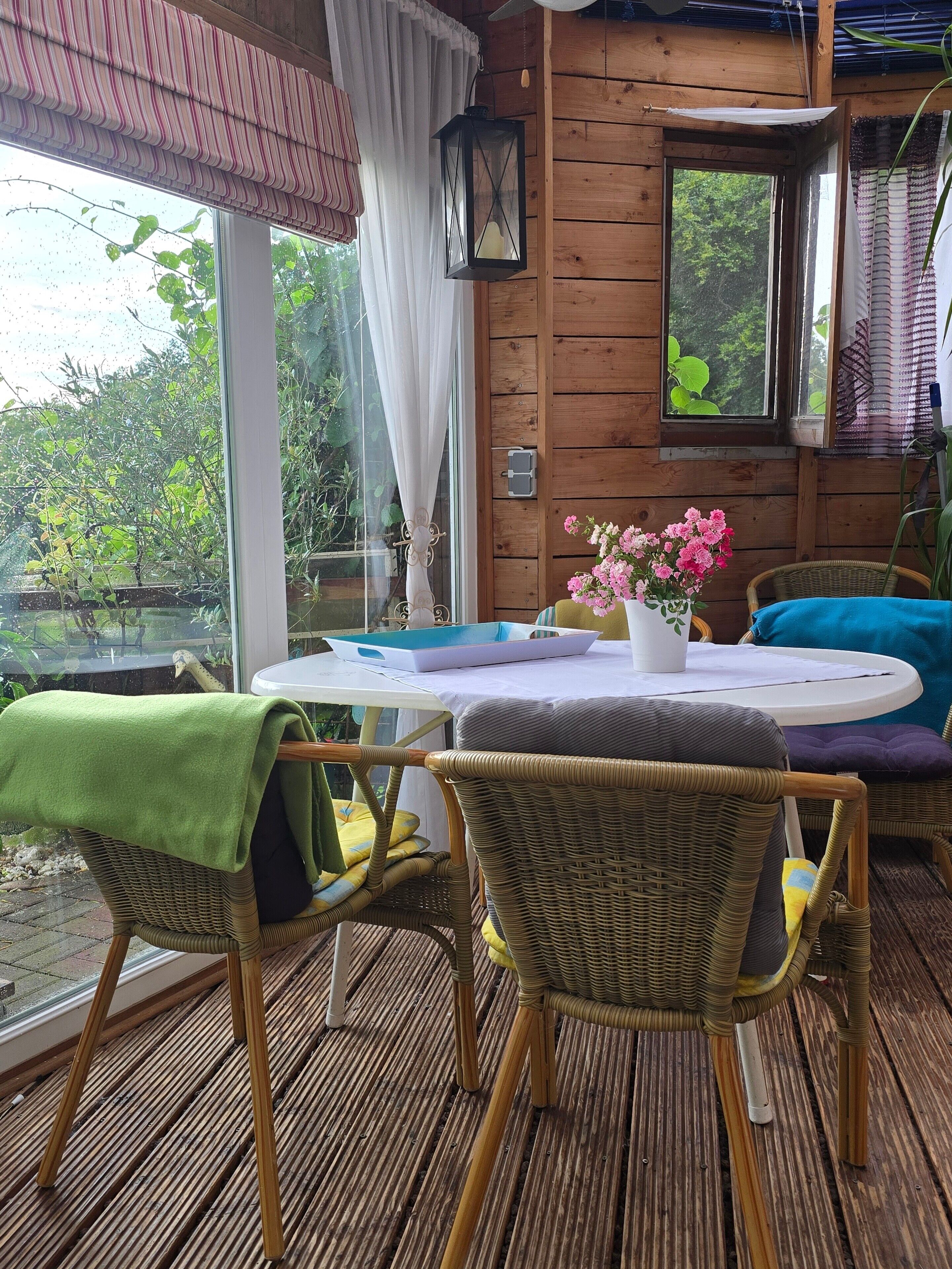 Eine Holzhütte mit Tisch, Stühlen und einem Fenster mit Blick ins Grüne.