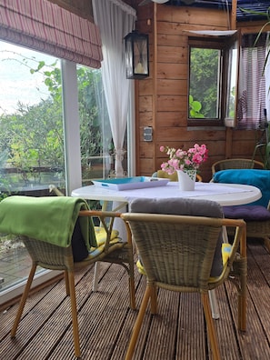 Una cabaña de madera con una mesa, sillas y un ventanal con vistas a follaje.