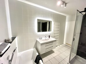 A modern bathroom with a large mirror, white tiles, a bathtub, a shower area, and a glass-enclosed shower.