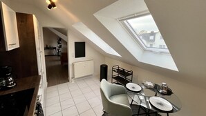 Um apartamento moderno estilo loft com claraboia, área de jantar com mesa de vidro e cozinha com fogão embutido.