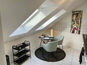A dining area with a table set for two, a black metal shelf unit, and a skylight above. - Apartment 'An-der-Aschaffaue' with Balcony and Wi-Fi (Aschaffenburg)