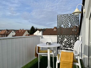 A balcony with a white table and chairs, a patterned screen, and a street view in the background. - Apartment 'An-der-Aschaffaue' with Balcony and Wi-Fi (Aschaffenburg)