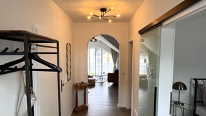 Um corredor com um cabideiro, uma mesa de madeira redonda e um lustre no teto.