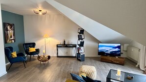 Uma sala de estar moderna em estilo loft, com teto inclinado, televisão de tela plana, mesa de centro e sofá.