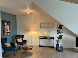 Una sala de estar moderna con techo inclinado, un cuadro, una lámpara de pie, una consola y una estantería.