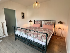 Un dormitorio con estructura de cama metálica, colcha estampada, dos lámparas de noche, una obra de arte en la pared y una puerta.