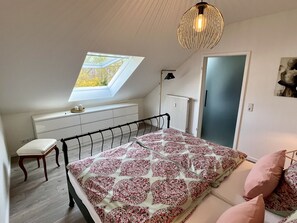 A bedroom with a skylight, a bed with patterned bedding, a chair, a desk, and a hanging light fixture. - Apartment 'An-der-Aschaffaue' with Balcony and Wi-Fi (Aschaffenburg)
