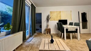 Un salon moderne avec un coin repas, de grandes fenêtres avec des rideaux, un radiateur et une vue sur l’extérieur.