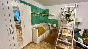 Une chambre avec un lit superposé, une armoire, une échelle, une plante et un bureau.