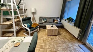 Un salon comprenant un canapé, une table basse, un fauteuil, une échelle et une grande fenêtre.
