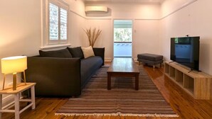 Ein modernes Wohnzimmer mit einer Couch, einem Couchtisch, einem Fernseher und einem Fenster mit Jalousien.