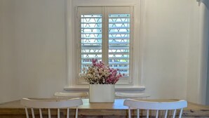 Ein Esstisch mit zwei weißen Stühlen und einer Blumenvase vor einem Fenster mit Jalousien.