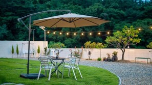 An outdoor patio with a metal table and chairs, an umbrella, and string lights. - Gyeongju Hanna Stay (Gyeongju)