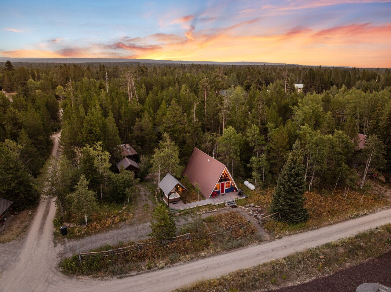 A cabin surrounded by dense forest, with a dirt road leading to it.