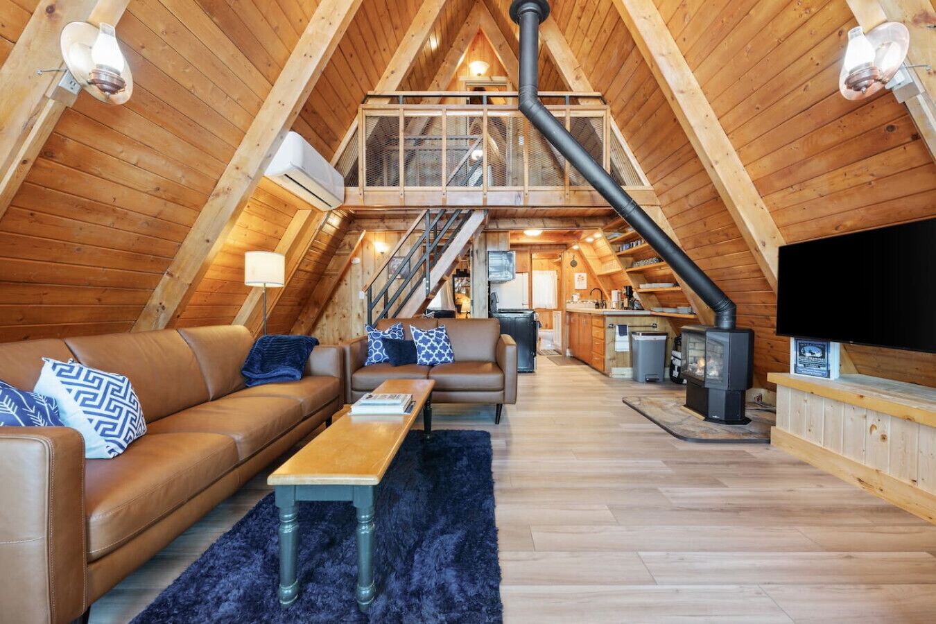 A cozy attic-style room with a wooden interior, a sofa, a coffee table, a TV, and a fireplace.