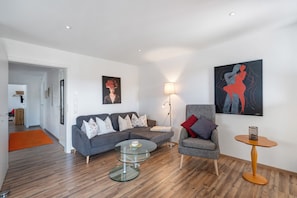 A modern living room with a grey sofa, a glass coffee table, a side table, and two paintings on the wall. - Apartment 'Helios' with Mountain View, Private Terrace and Wi-Fi (Freiamt)
