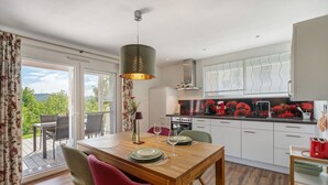 Una cucina moderna con mobili bianchi, un'area pranzo con tavolo e sedie in legno e vista attraverso la porta in vetro.