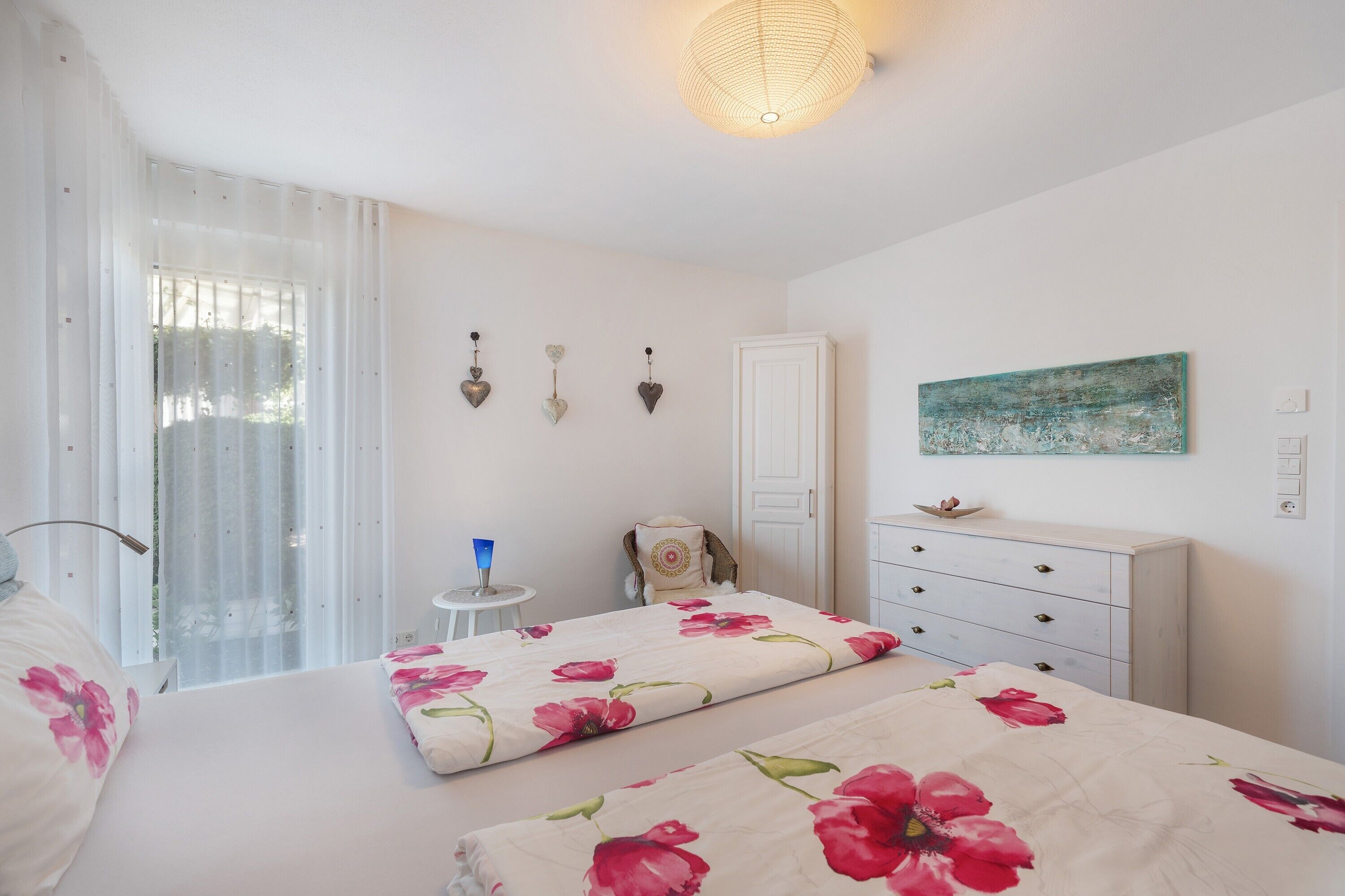 Une chambre avec deux lits, une table de chevet, une commode, une œuvre d’art accrochée au mur et une porte.