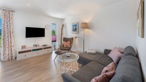 Uma sala de estar moderna com uma televisão de tela plana, um sofá, uma poltrona, um abajur e uma pequena mesa.
