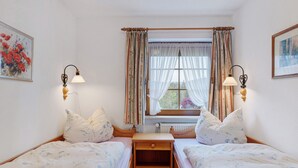 A bedroom with two beds, a window with curtains, wall-mounted lamps, and a radiator.