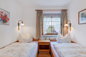 A bedroom with two beds, a window with curtains, wall-mounted lamps, and a radiator.