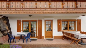 A building with a balcony, wooden doors, a round table with chairs, and a bench.