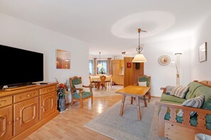 Ett vardagsrum med en tv, trämöbler, en matplats och ett kök i bakgrunden.
