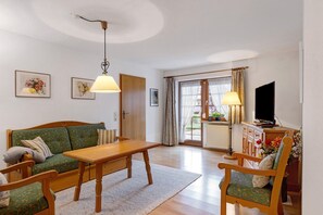 Ett vardagsrum med en soffa, ett träbord, en stol, en tv och ett fönster med gardiner.