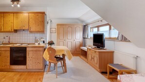 A kitchen with wooden cabinets, a dining table with chairs, a small TV, and a window with curtains.