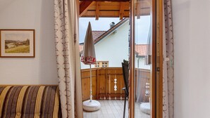 A room with a wooden ceiling, a framed picture on the wall, a striped sofa, and a view of a balcony with a white umbrella.