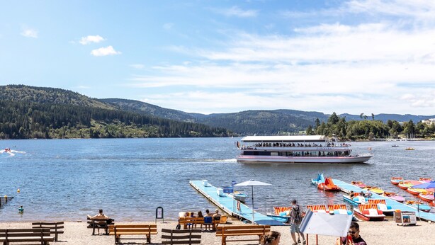 A lakeside view with a boat, benches, and a dock with colorful canoes.