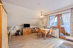 Une pièce chaleureuse avec un plancher en bois, une table à manger avec des chaises, un téléviseur, un radiateur et une fenêtre avec des rideaux.