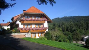 A two-story building with balconies, surrounded by greenery and a forested hill.