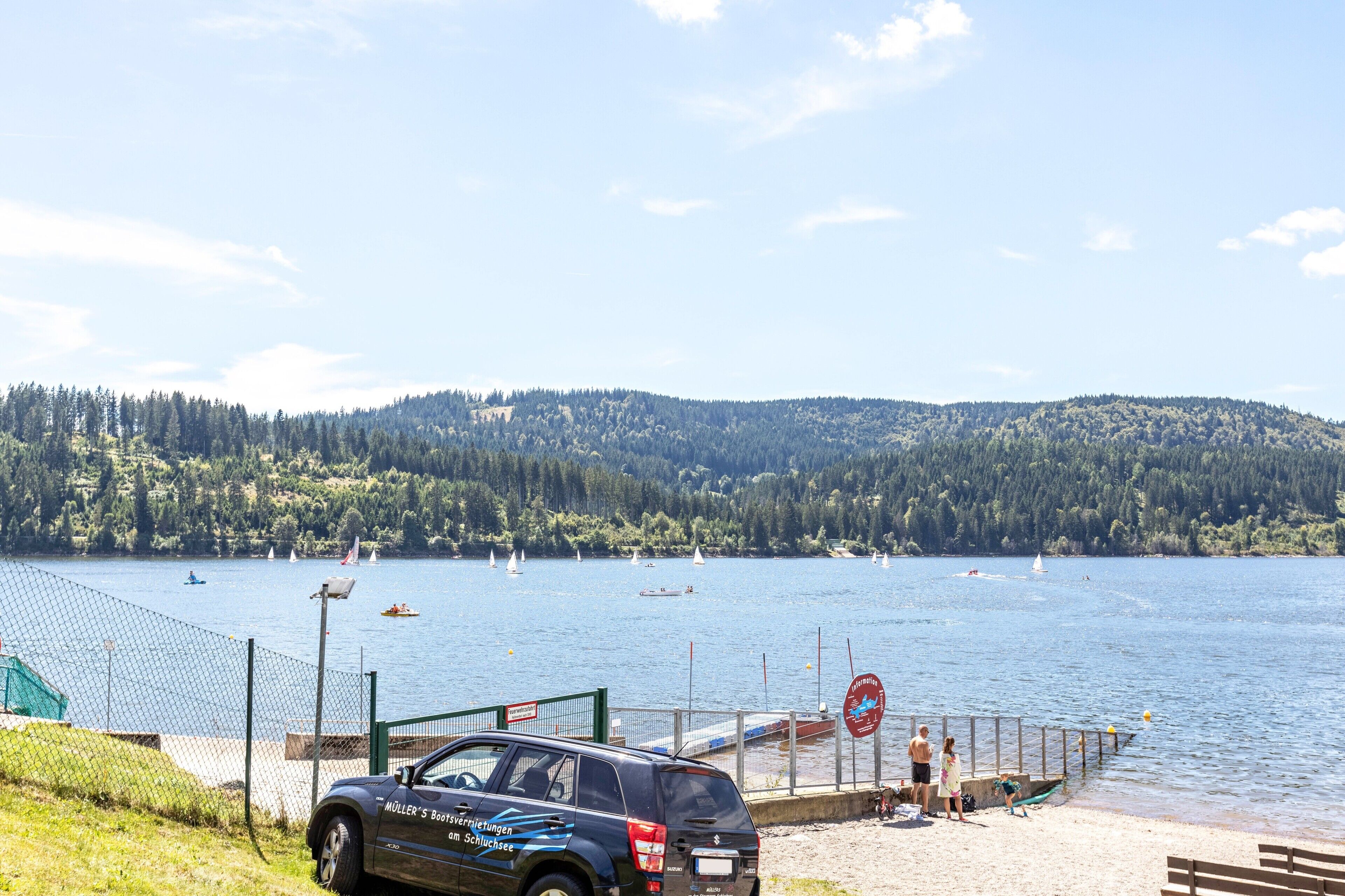 Un lac avec des voiliers, une voiture et une clôture verte.