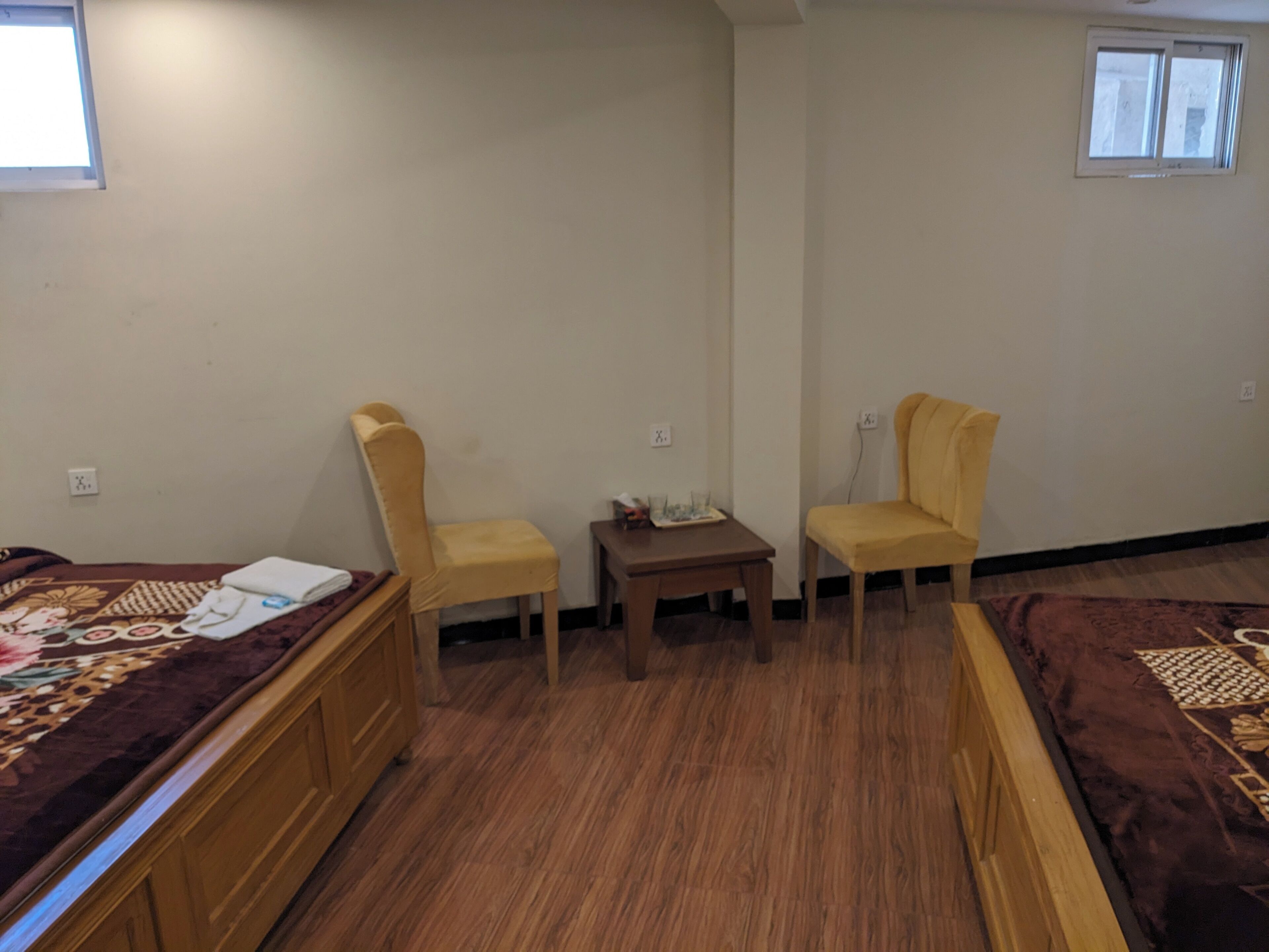 A room with two yellow chairs, a small wooden table, a bed with a patterned bedspread, and a window.