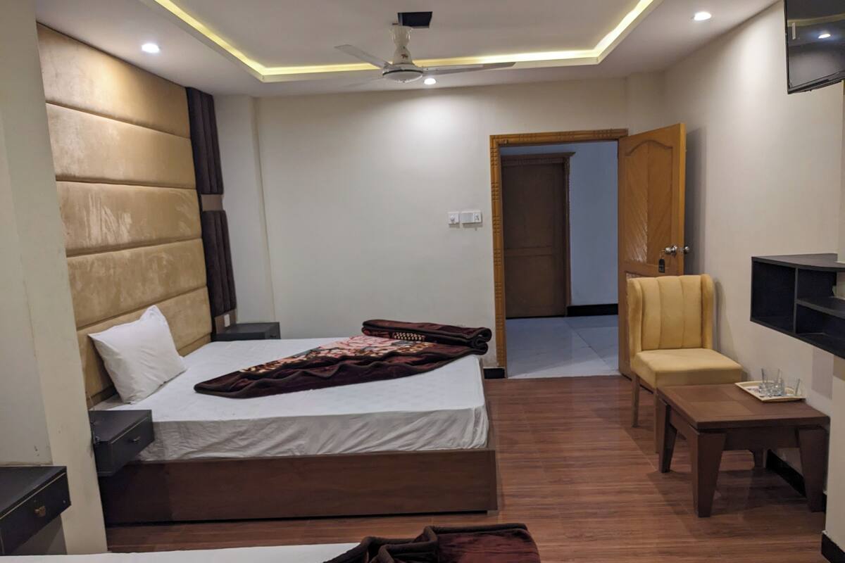 Ein modernes Hotelzimmer mit einem großen Bett, einem Nachttisch, einem Sessel und einem flachbildfernseher an der Wand.