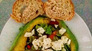 Ein Teller mit einem Salat aus Avocado, Salat, Tomaten und zerbröseltem Käse, dazu zwei Brotscheiben.