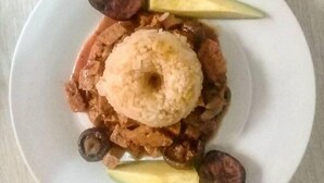 Ein Teller mit einer Reis-Beilage, umgeben von Avocadoscheiben und zwei runden Bestandteilen, möglicherweise Früchte oder Gemüse.