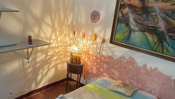 Ein Schlafzimmer mit einem Bett, einem Nachttisch mit Lampe, einem Bild an der Wand und einem Fenster, das Schatten wirft.
