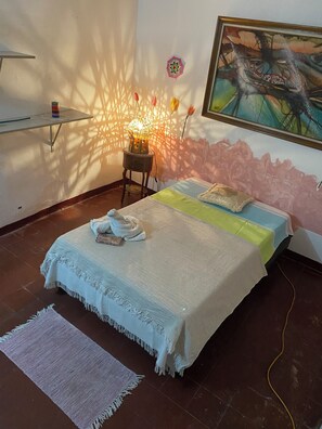 Une chambre à coucher avec un lit, une table de chevet avec une lampe, un tableau accroché au mur et une fenêtre qui projette des ombres.