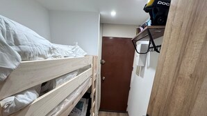 Um corredor estreito com uma cama beliche à esquerda e uma porta no final.