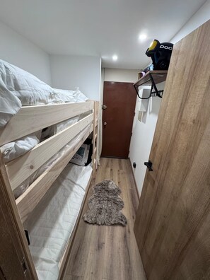 Un pasillo estrecho con una litera a la izquierda y una puerta al final.