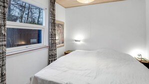 A bedroom with a large bed, a window with curtains, a wall-mounted light, and a ceiling light fixture.