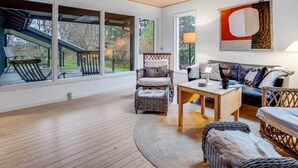 A spacious living room with large windows, a wooden ceiling, and a view of a deck.