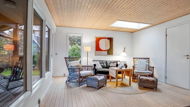 A cozy living room with a wooden ceiling, large windows, and wicker furniture.