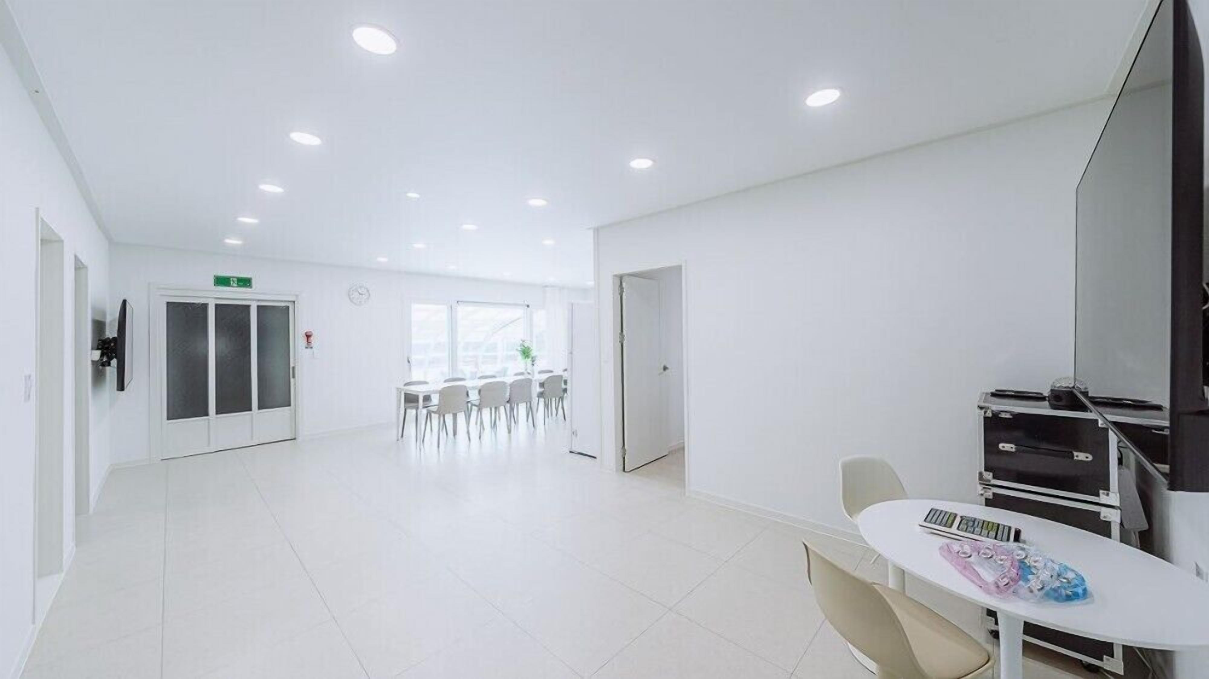 Una habitación amplia y bien iluminada con una mesa grande y sillas, una puerta que da a otra área, y un extintor visible.
