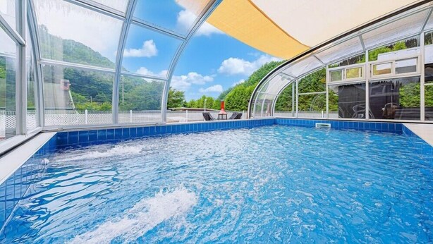 Una piscina interna con pareti di vetro trasparente, pavimento in piastrelle blu e vista su del verde all'esterno.