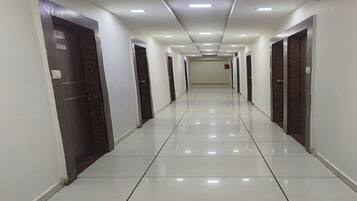 A long, narrow hallway with white tiled floors and walls, featuring multiple doors on either side.
