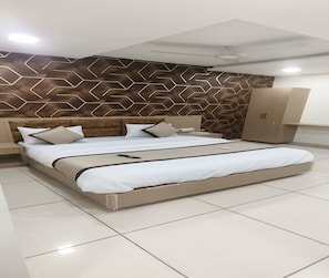 A modern hotel room with a large bed, a headboard with a geometric pattern, a wardrobe, and a ceiling light.